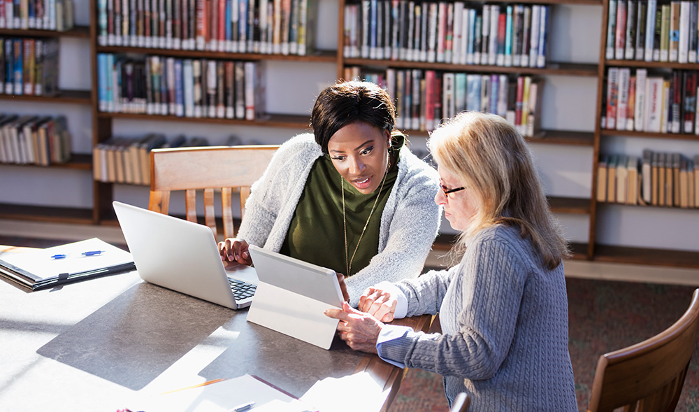 Two people working on laptops in a library